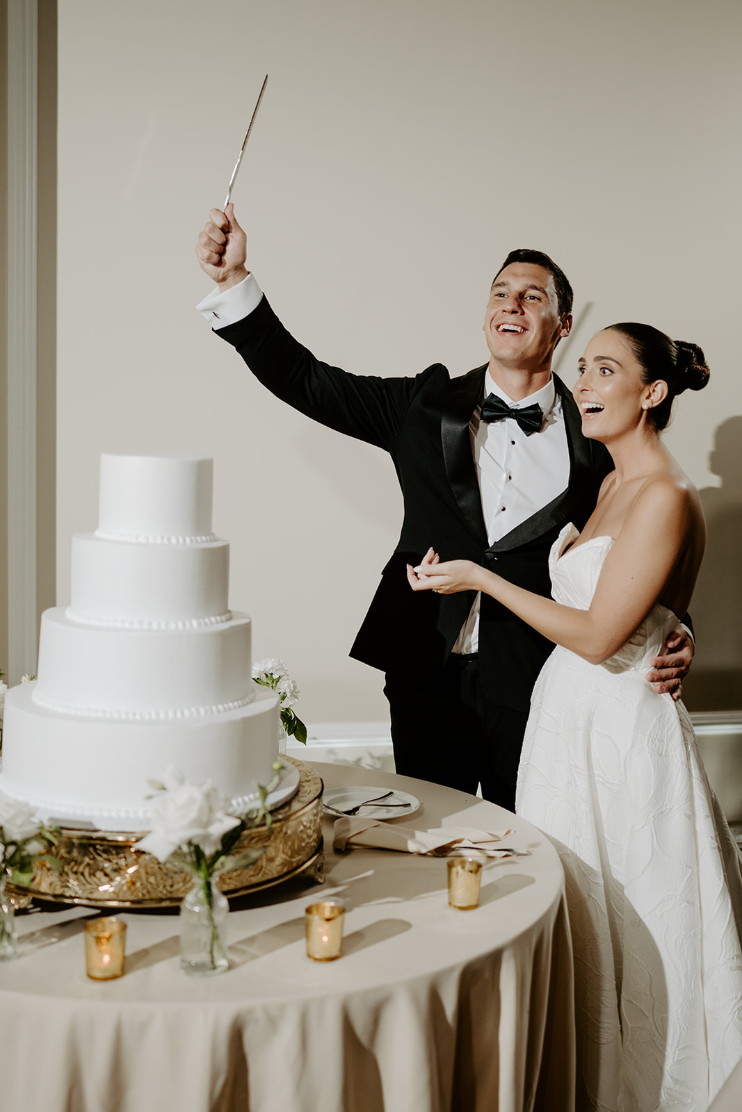 Bride and groom sharing a joyful laugh as the groom raises the cake knife before cutting the cake.